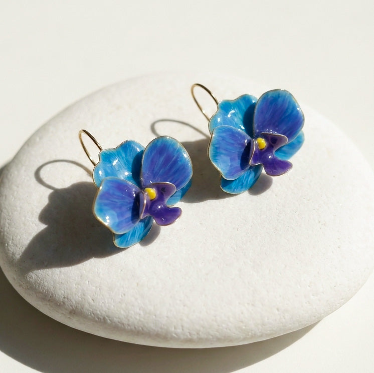 Blue and purple orchid flower-shaped earrings on a white stone surface