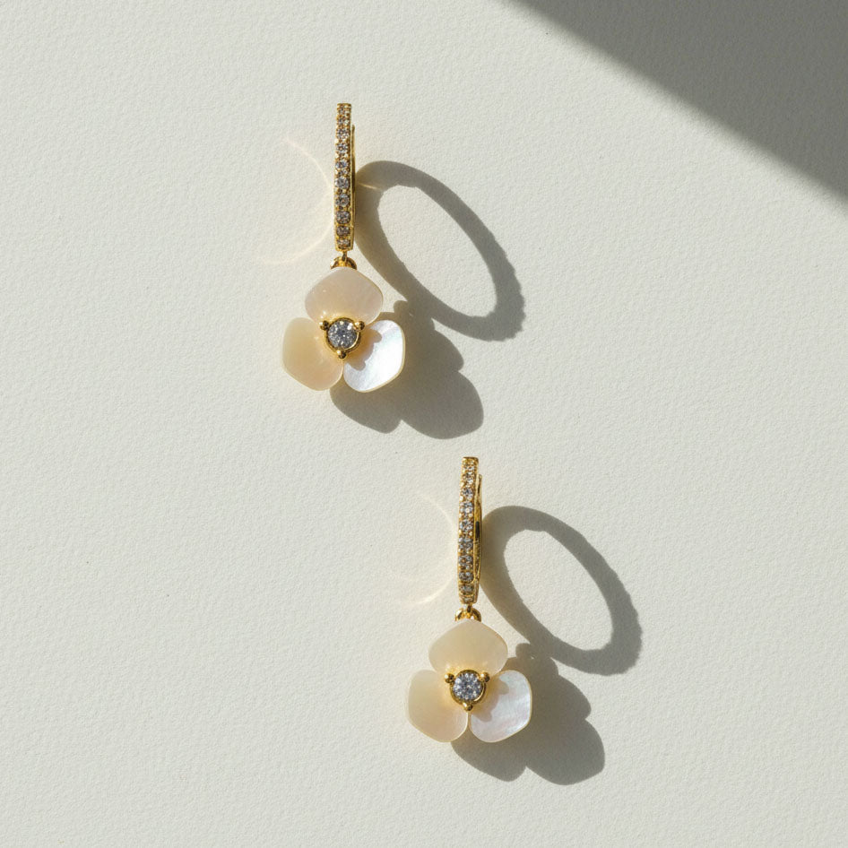 Gold hoop earrings with mother-of-pearl flower drops on white background