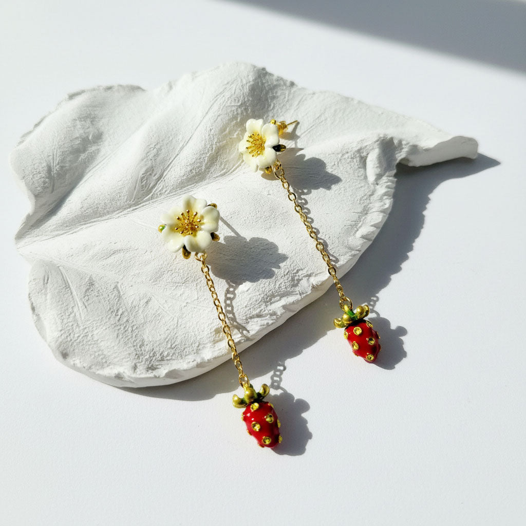Pair of earrings with floral and strawberry designs on a white leaf