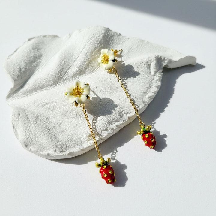 Pair of earrings with floral and strawberry designs on a white leaf