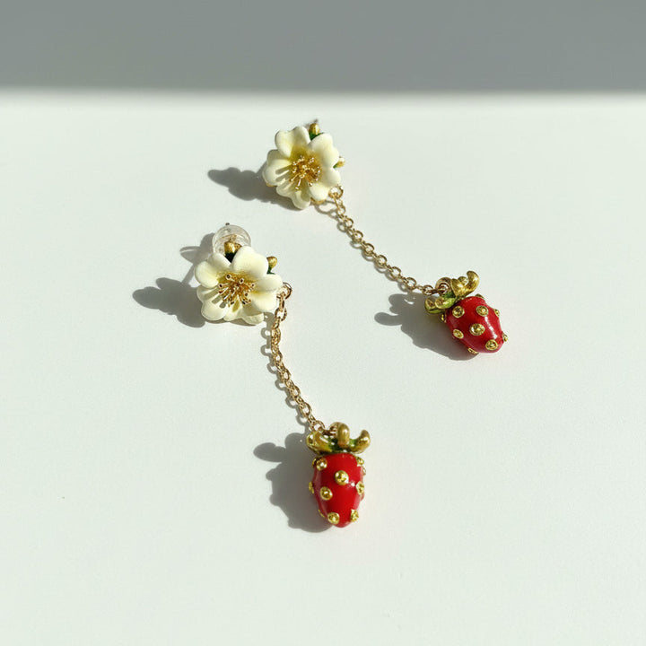 Pair of earrings with strawberry and flower designs on a white background