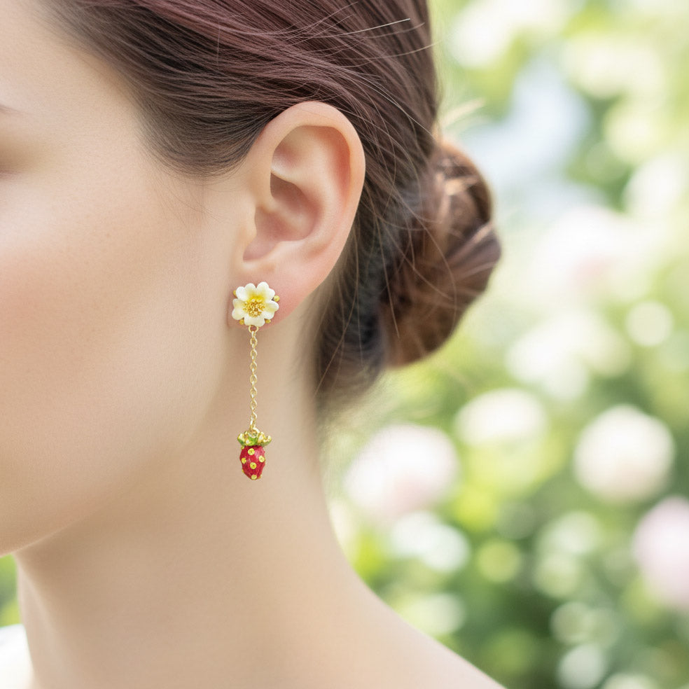 Earring with a strawberry and flower design worn by a person outdoors.