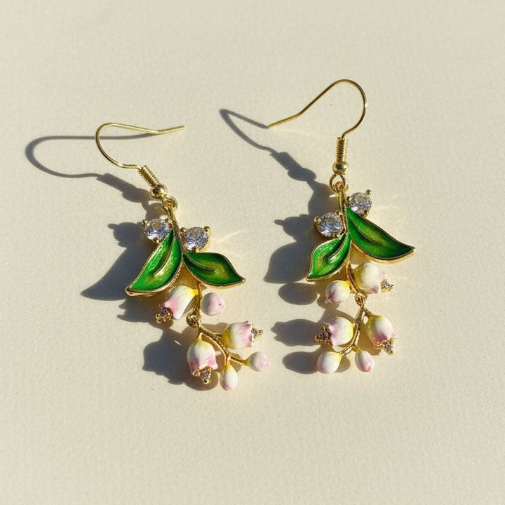 Gold earrings with green leaves and pink lily flowers on a beige background