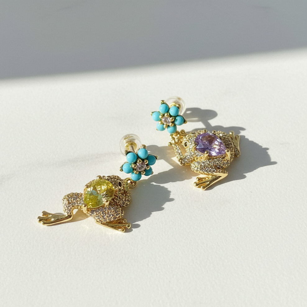 Gold frog earrings with turquoise flower studs and colorful glass stones on white background.