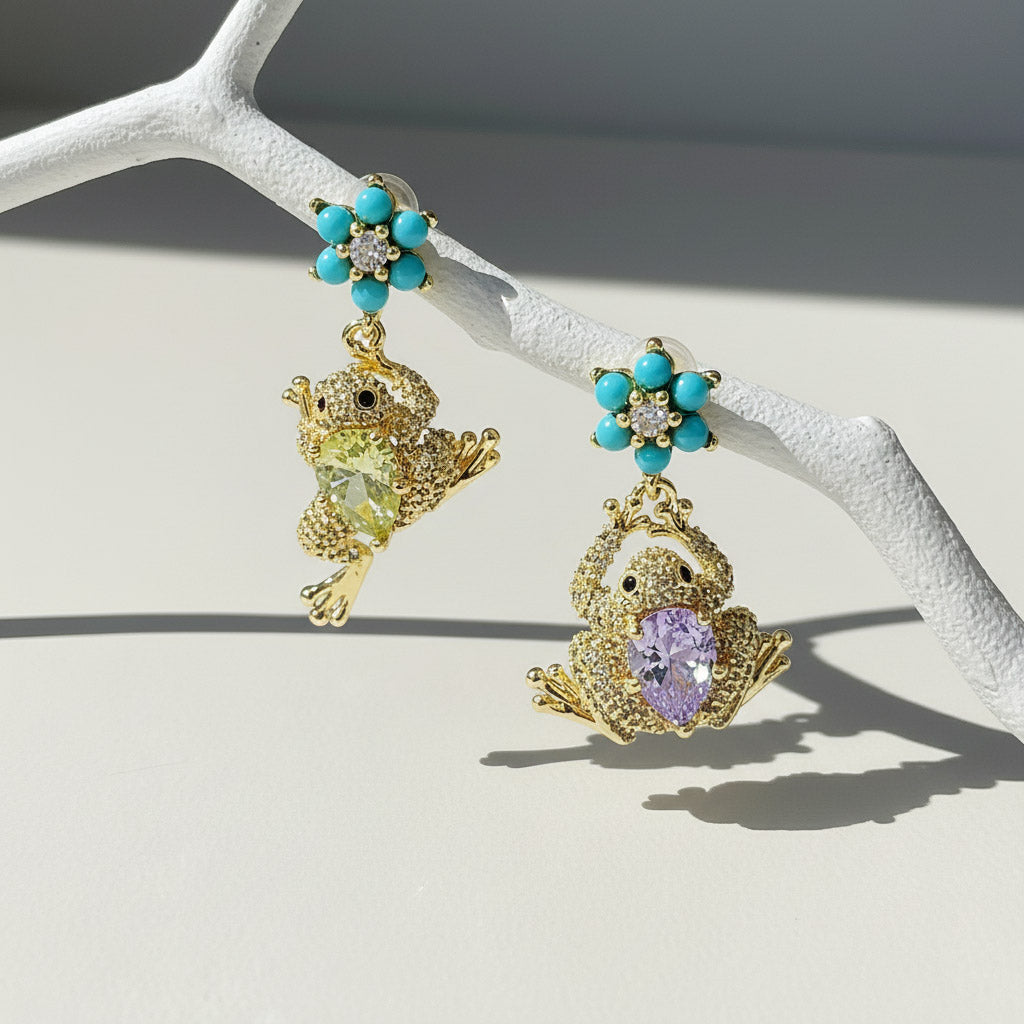 Frog-shaped drop earrings hanging from turquoise flower studs in sunlight.