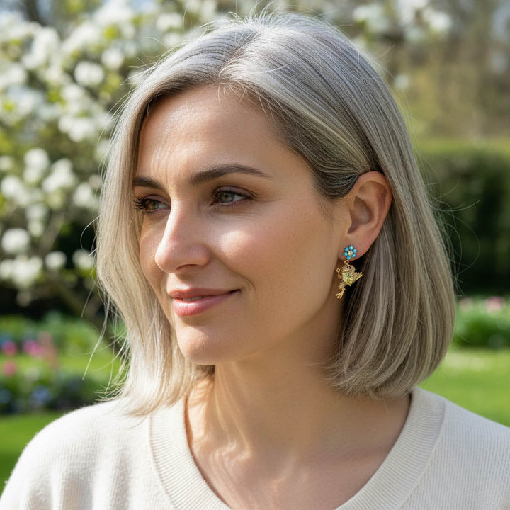Model wearing gold frog earrings with turquoise flower studs outdoors.