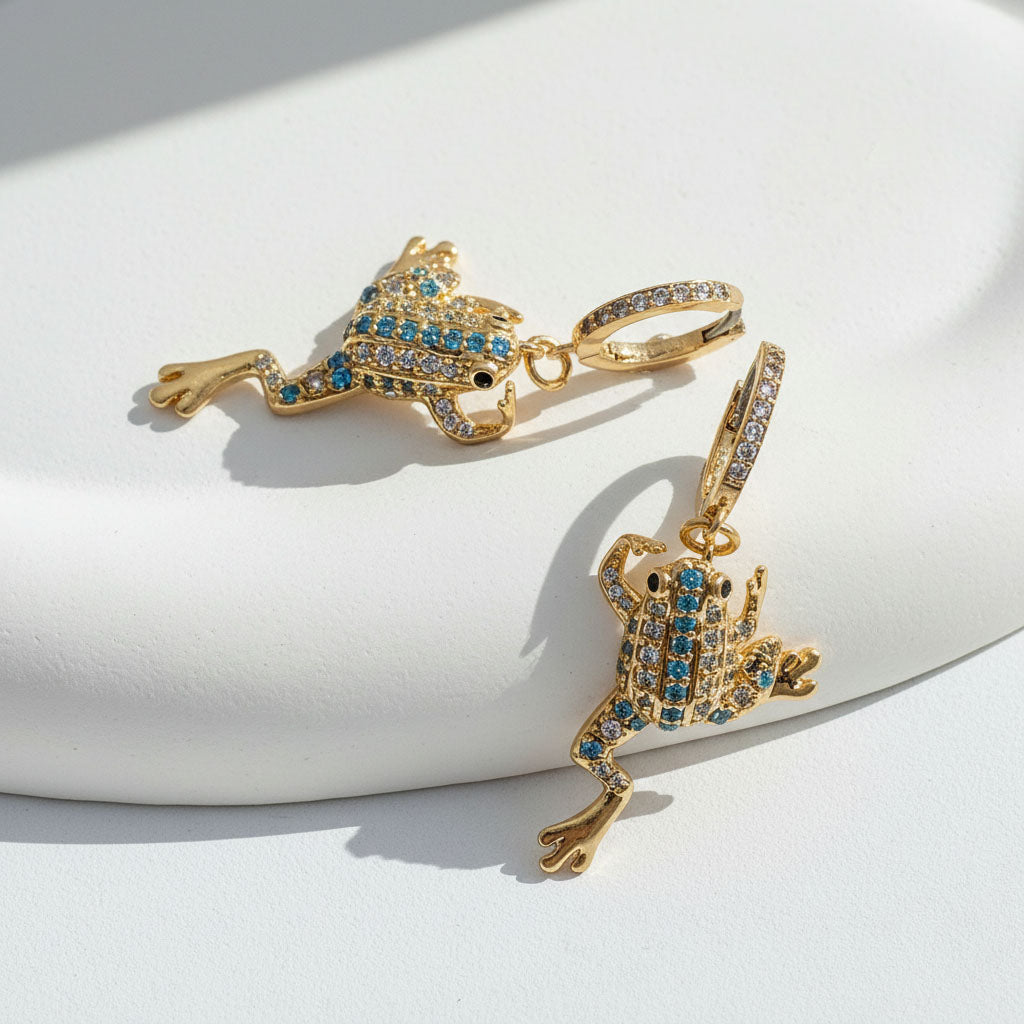 Gold frog-shaped earrings with blue gemstones on a white surface