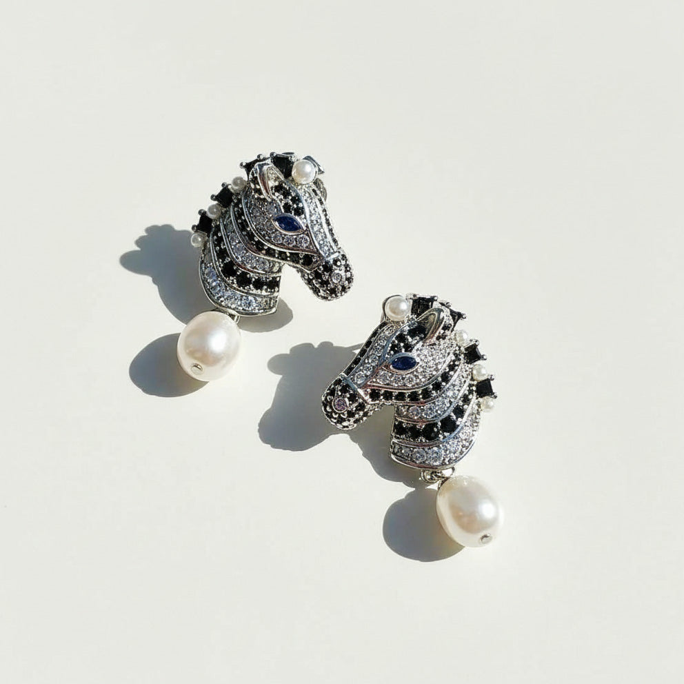 Pair of horse-shaped earrings with pearl drops on a light background
