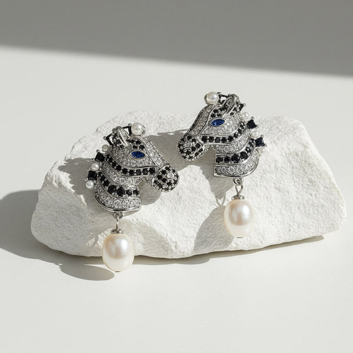 Pair of ornate earrings with pearls on a textured white surface
