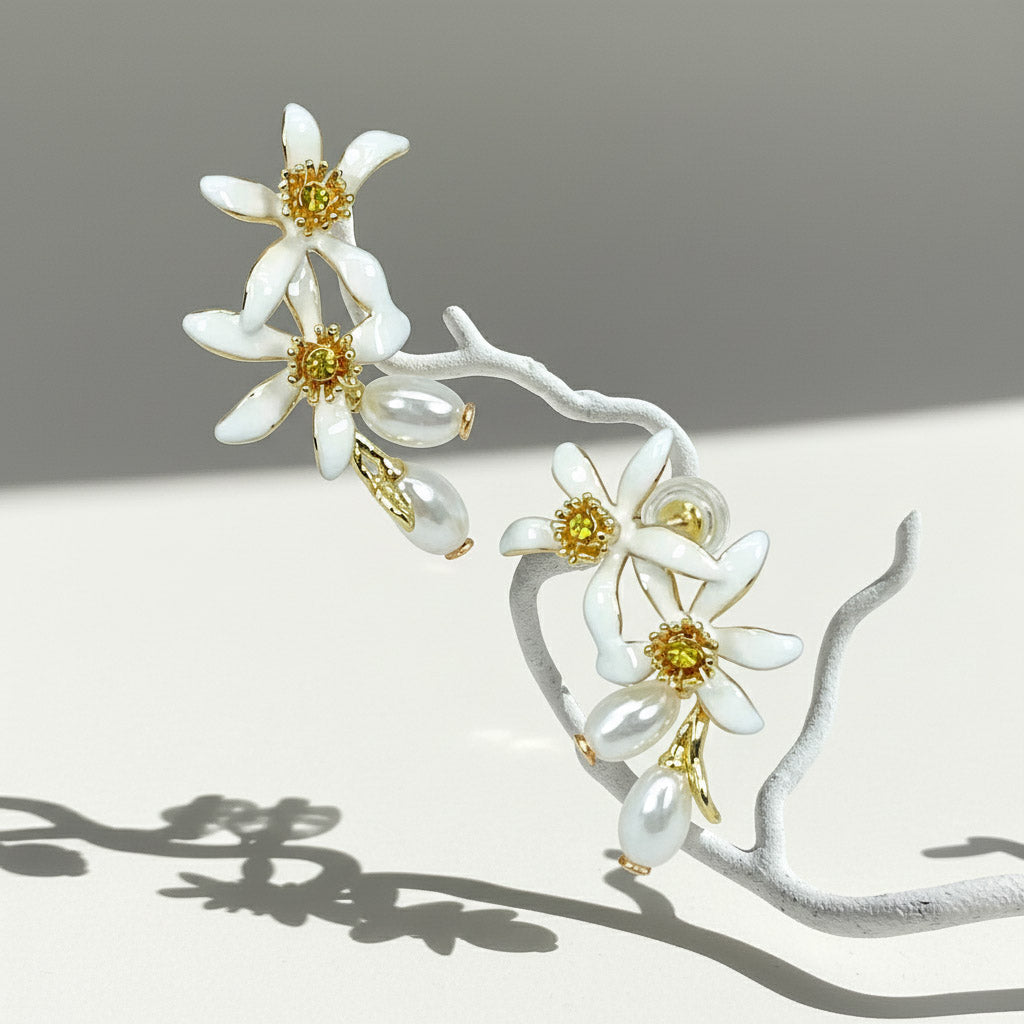 Enamel flower earrings with pearls hanging on white branch.