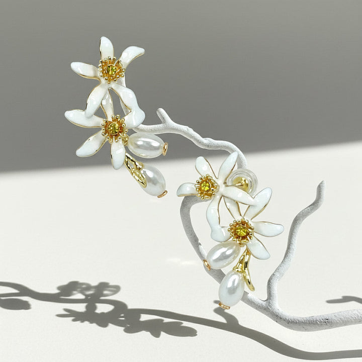 Enamel flower earrings with pearls hanging on white branch.