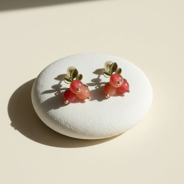 Pair of earrings resembling red berries on a white stone with a beige background