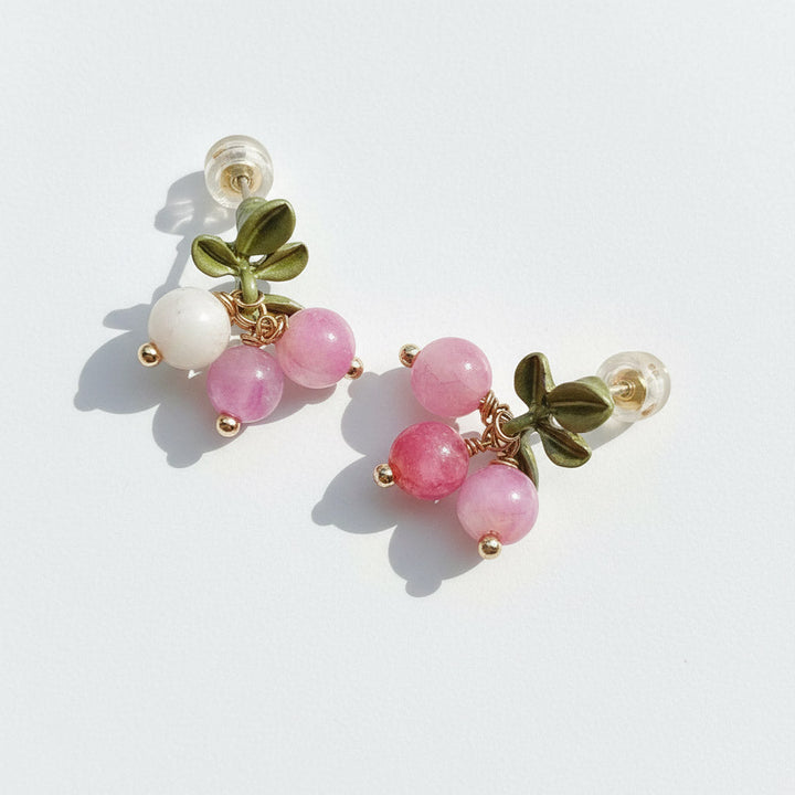 Pair of earrings with pink beads and green leaves on a white background