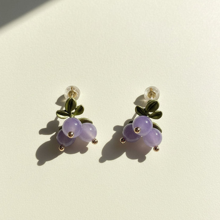 Pair of earrings with purple berries and green leaves on a beige background