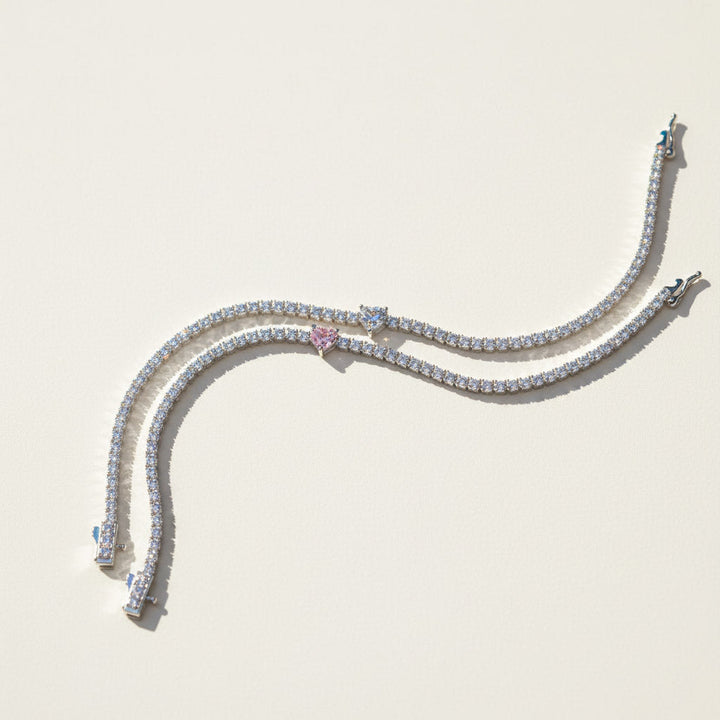 Two moissanite heart tennis bracelets in pink and white center stones on a light background