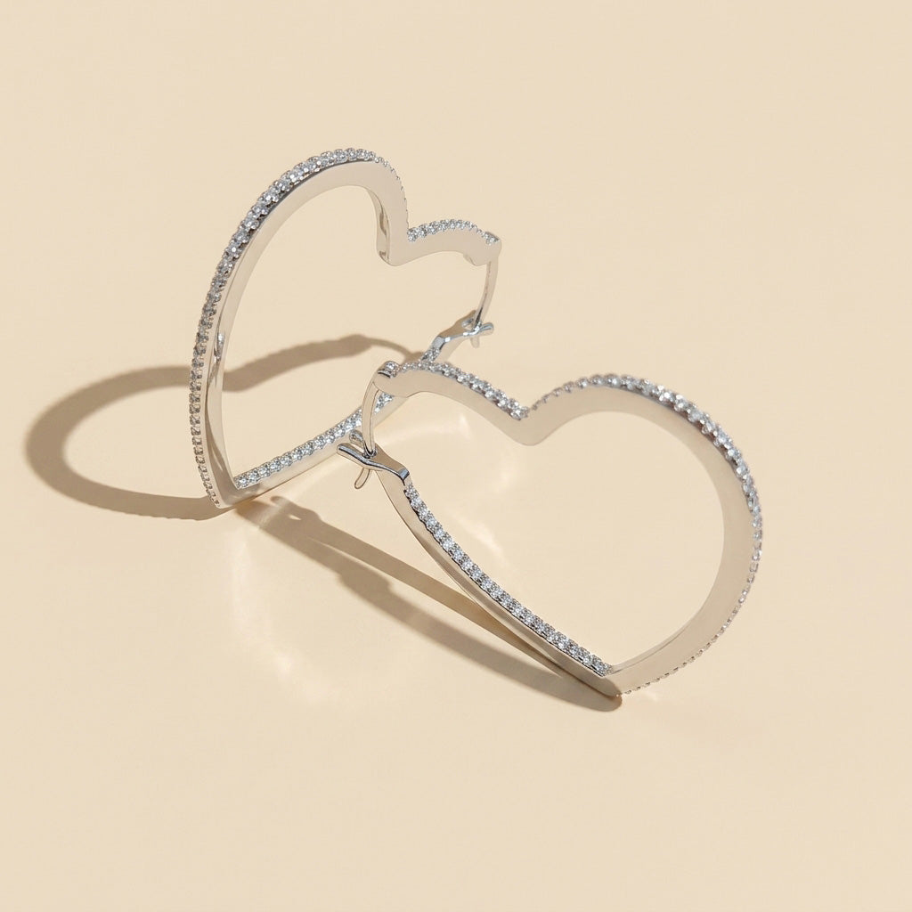 Heart-shaped silver hoop earrings with moissanite on a beige background