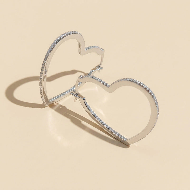 Heart-shaped silver hoop earrings with moissanite on a beige background