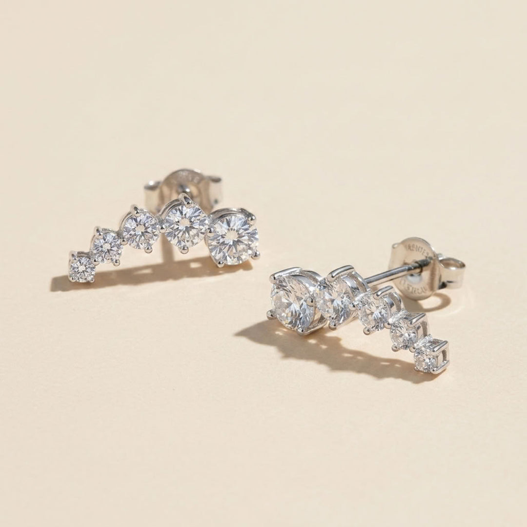 Pair of curved moissanite ear climber earrings with five graduated round stones in cream color background