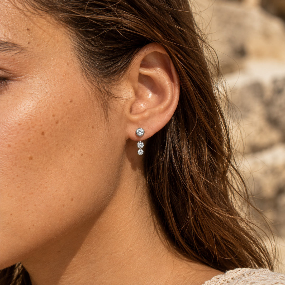Silver three-stone moissanite ear jacket earring worn on the earlobe in natural sunlight