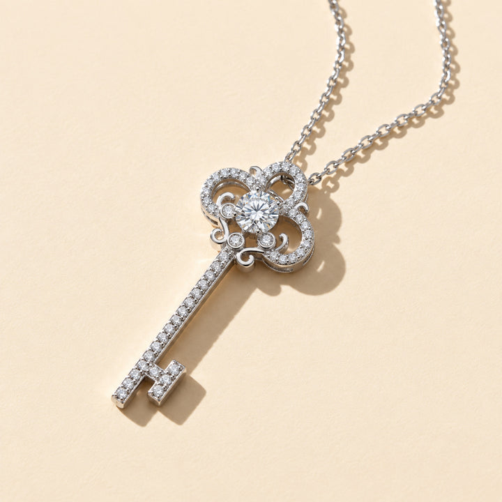 Close-up of ornate moissanite key necklace with round center stone and scrollwork detailing, shown on a warm beige background.