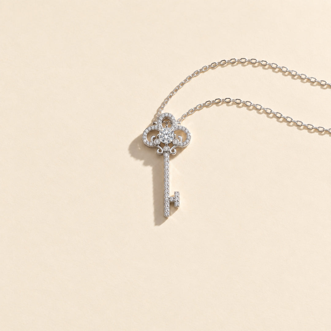 Full view of ornate moissanite key pendant necklace in platinum-plated sterling silver, resting on a light beige background.