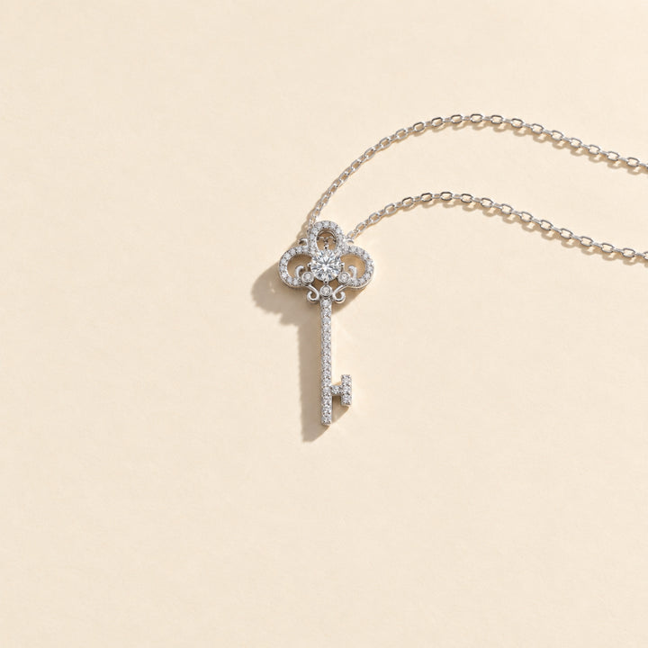 Full view of ornate moissanite key pendant necklace in platinum-plated sterling silver, resting on a light beige background.