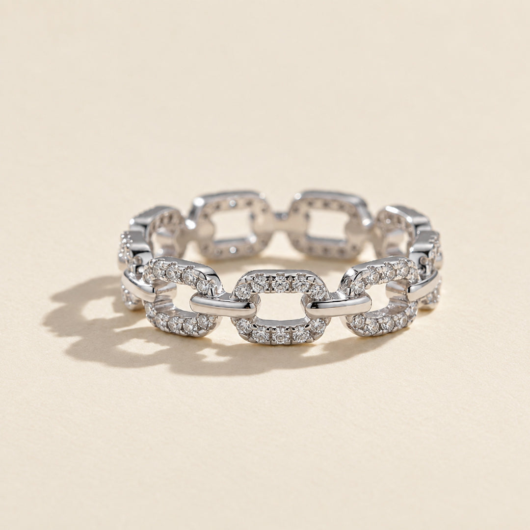 Front view of pavé chain-link moissanite ring with polished silver connectors, photographed on a warm beige background with a soft shadow.