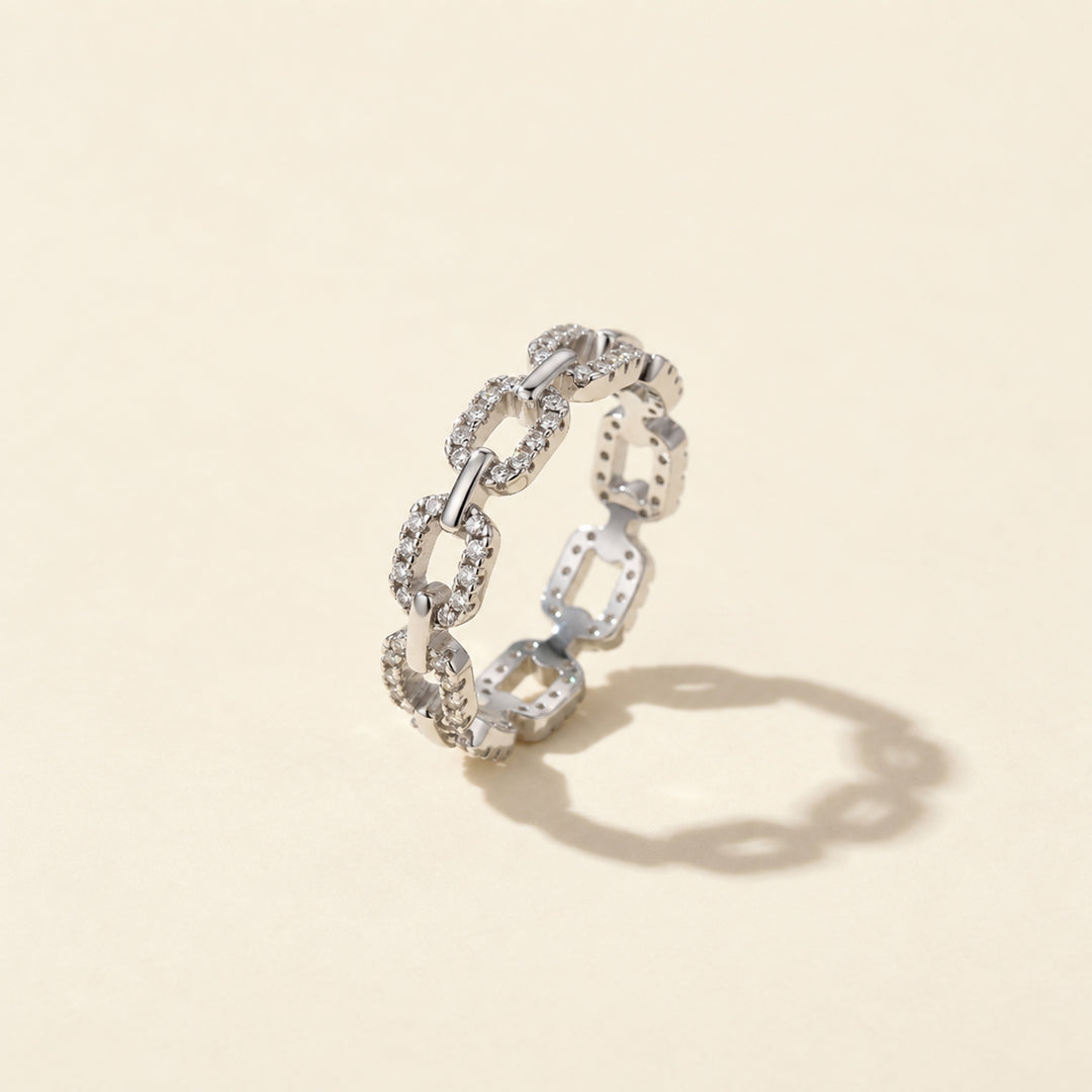 Pavé chain-link moissanite ring, photographed on a warm beige background with a soft shadow.