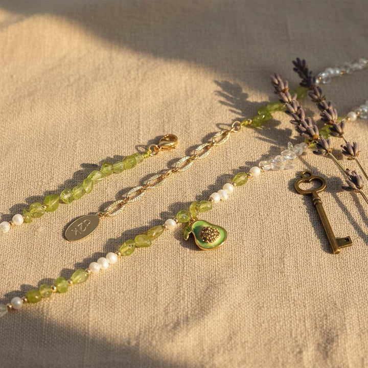 Necklace with green beads, white pearls, and a key charm on a beige fabric background