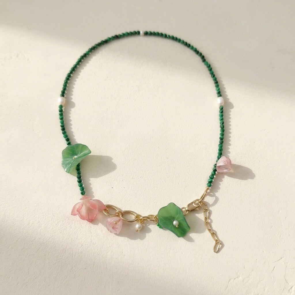 Green malachite and pink blossom beaded necklace with pearls on white background.