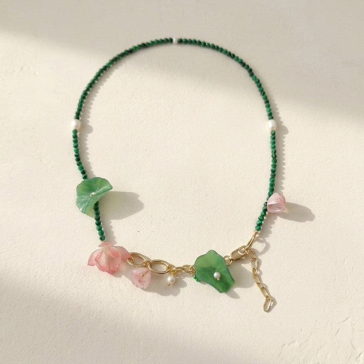 Green malachite and pink blossom beaded necklace with pearls on white background.