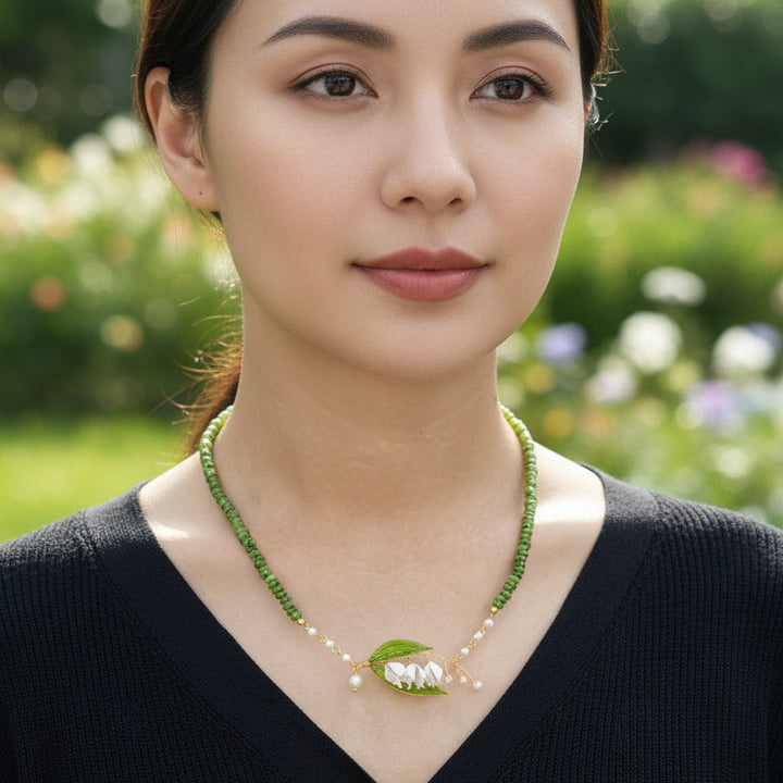 Woman wearing a green beaded necklace with a leaf design in a garden setting