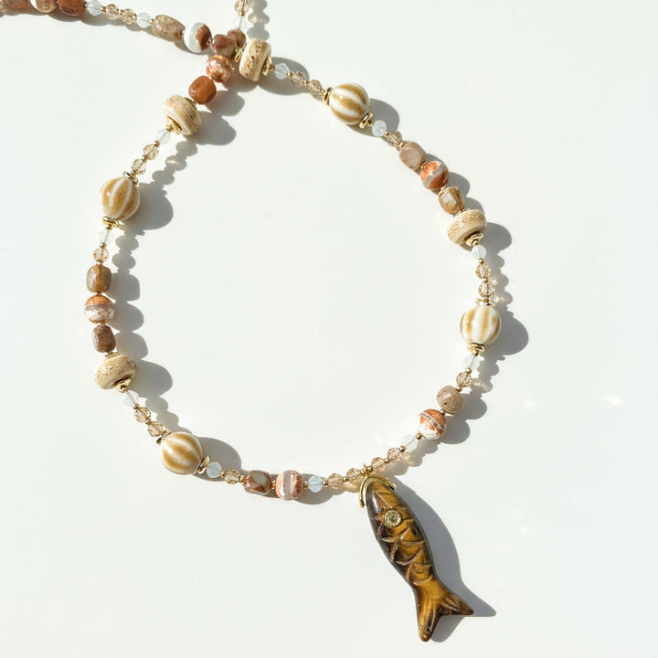 Crafted beaded necklace with brown ceramic beads and carved fish pendant on white background