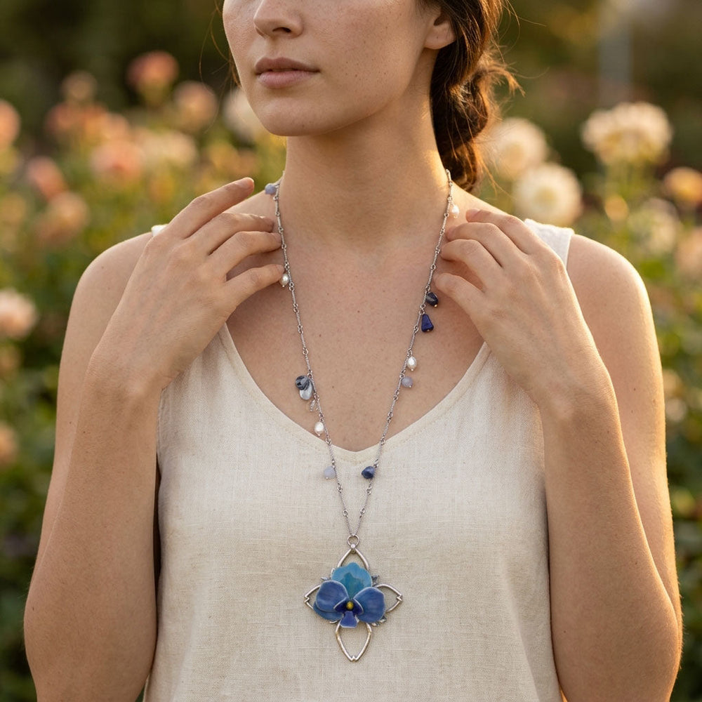 Woman wearing a necklace with a blue orchid flower pendant in a natural setting