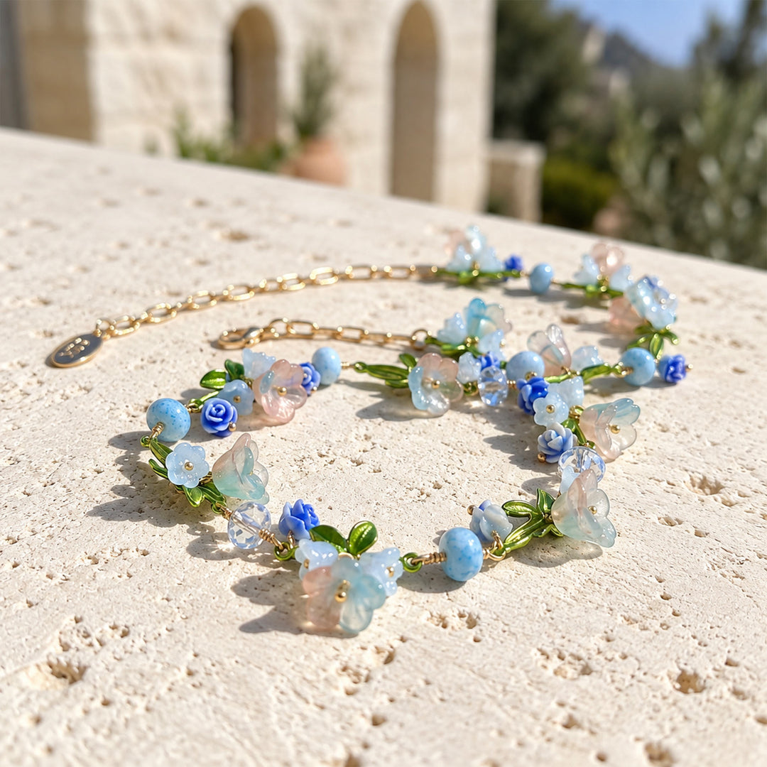 Handcrafted pastel garden necklace with blue and blush flowers arranged on a pale mineral stone slab.