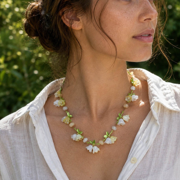 Woman wearing Woman Wearing Spring Blossom Garden Necklace with Glass Flowers and Enamel Leaves with a blurred green background