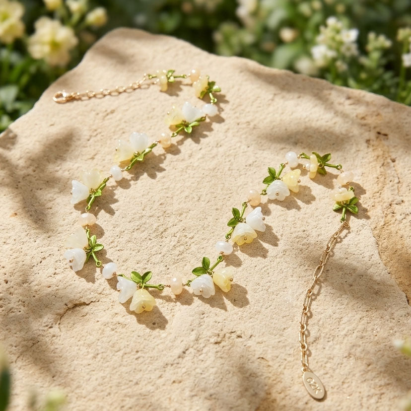 Spring Blossom Garden Necklace with Glass Flowers, Semi-Precious Stones and Enamel Leaves on a textured surface with greenery in the background
