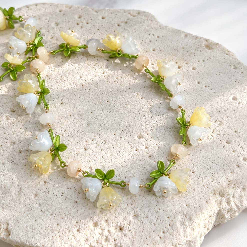 Close-Up of Handcrafted Floral Necklace with Glass Bellflowers and Green Enamel Leaves on a textured stone surface