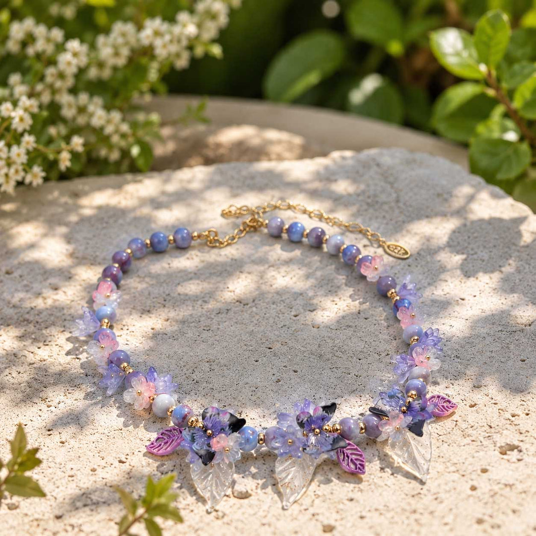 Butterfly Floral Statement Necklace with Glass Blossoms on a stone surface with greenery in the background