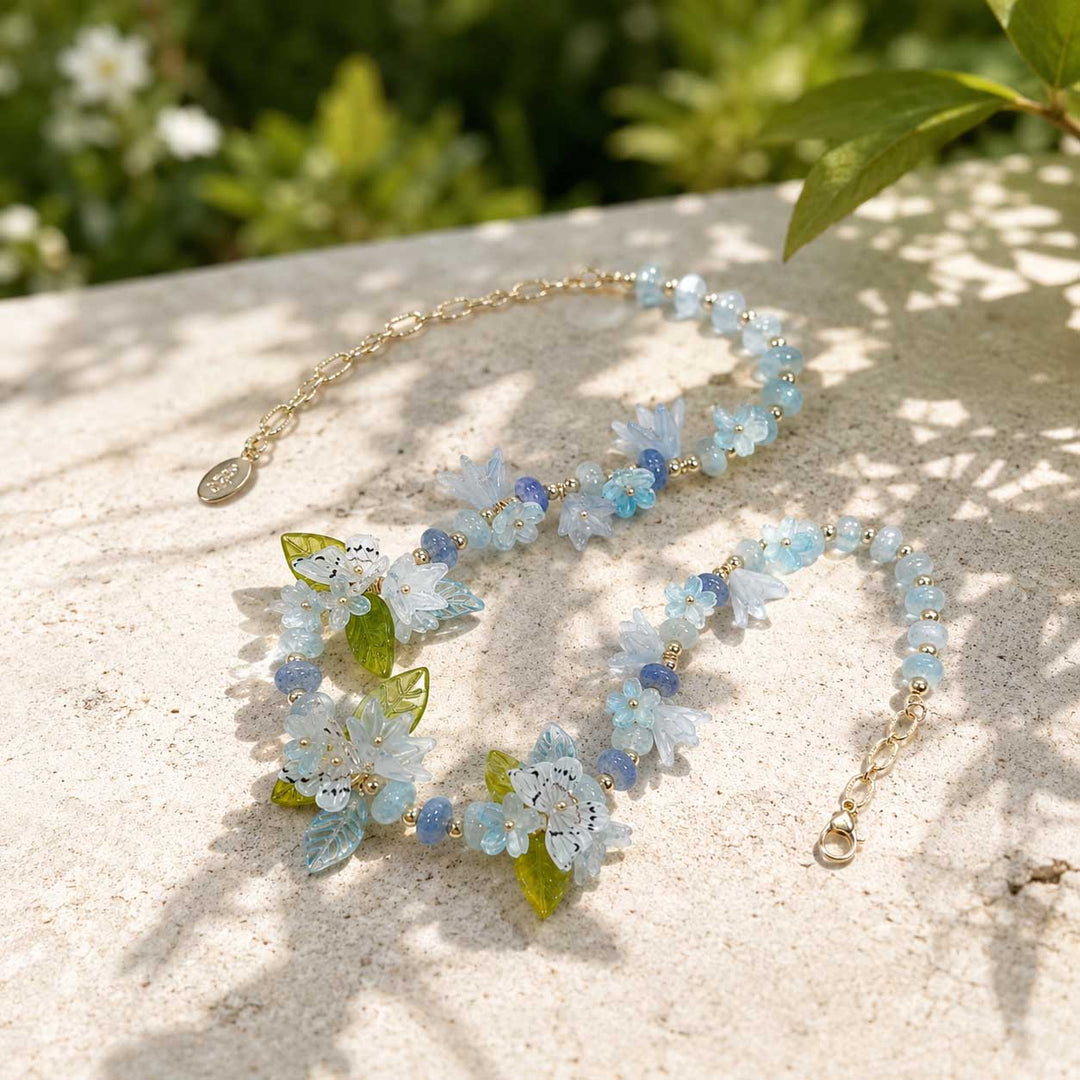 Botanical butterfly floral statement necklace with blue and lavender tones on a light surface with greenery in the background