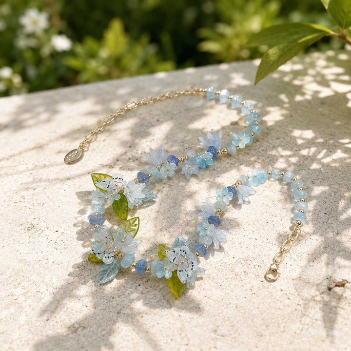Botanical butterfly floral statement necklace with blue and lavender tones on a light surface with greenery in the background