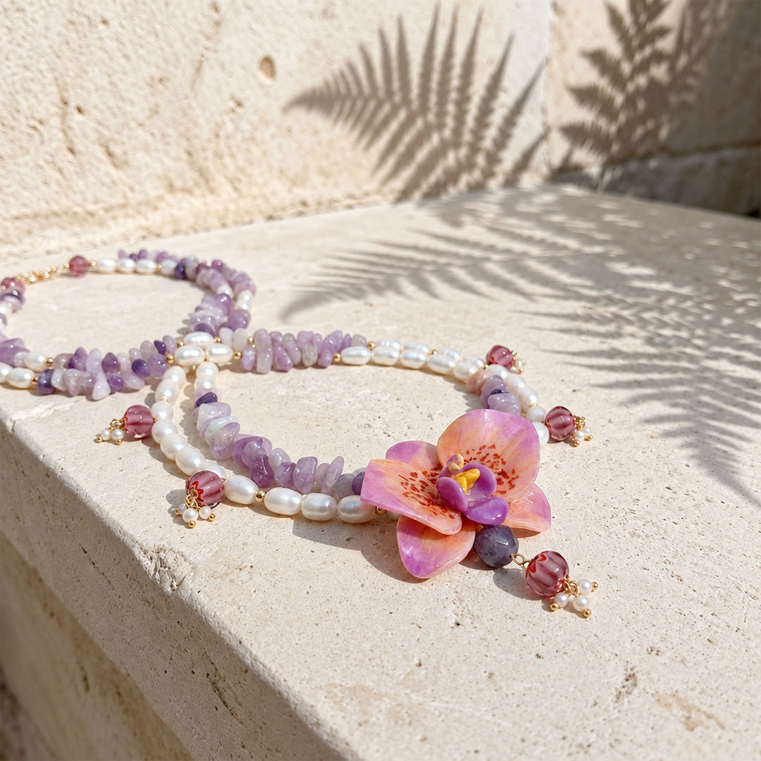 Orchid statement necklace with purple jade, freshwater pearls and lampwork glass beads, displayed on a textured stone surface in warm sunlight with palm leaf shadows.
