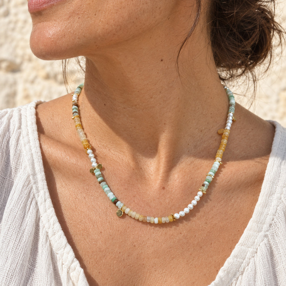 A close-up of a woman wearing a delicate beaded necklace with Chrysoprase, Yellow Jade and freshwater pearl necklace with delicate gold accents, paired with a white top.