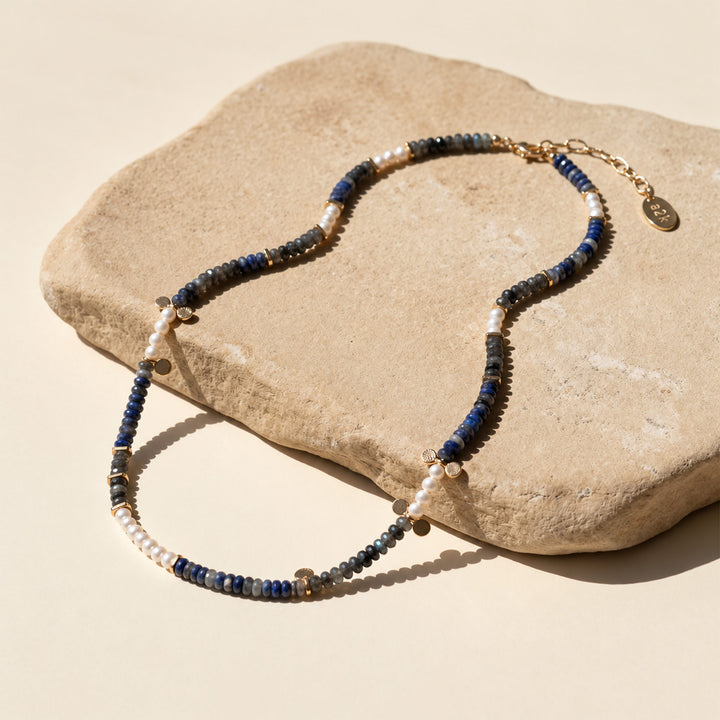 Full mixed gemstone necklace with Black Labradorite, Sodalite, freshwater pearls and gold extender chain, displayed on rock.