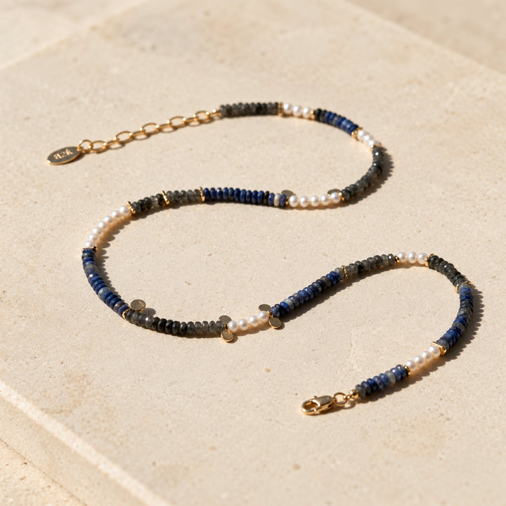 Black Labradorite, Sodalite and freshwater pearl necklace with gold accents displayed on limestone in sunlight