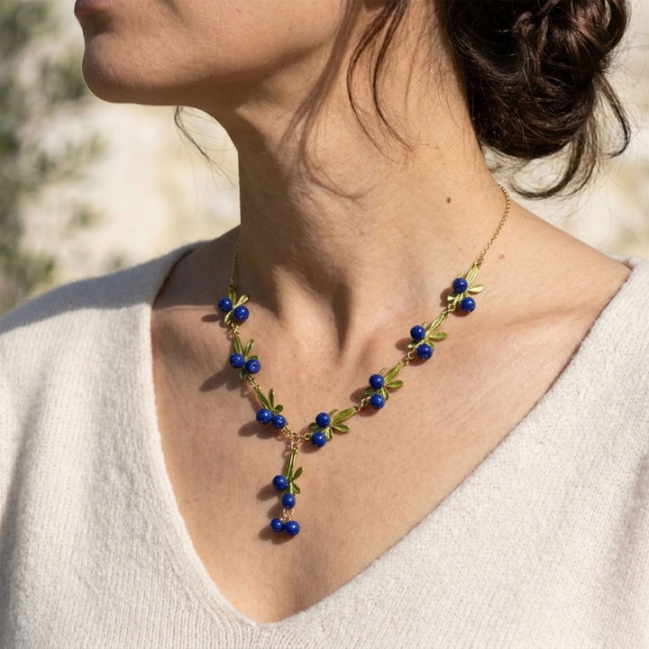 Blueberry garden enamel necklace with cobalt blue berry clusters and green leaves worn by a model outdoors.