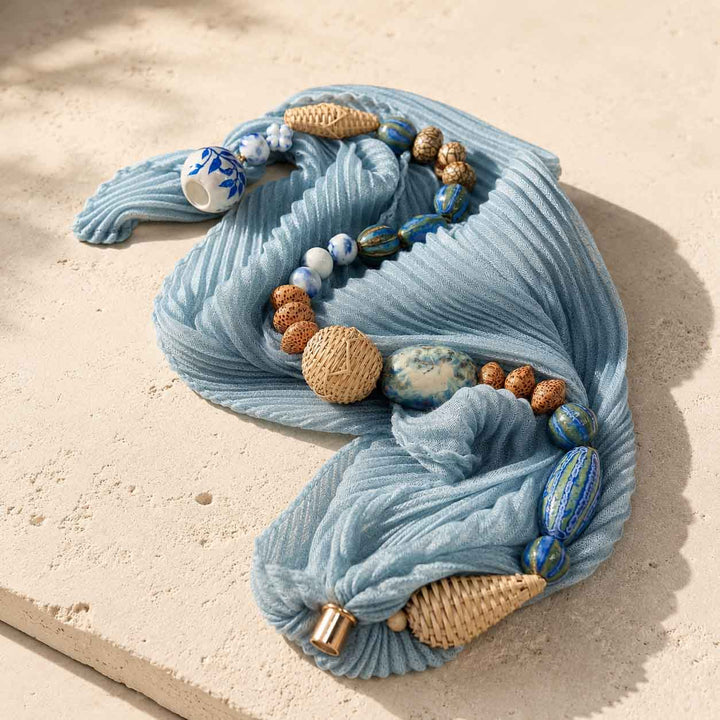 Close-up of artisan pleated scarf necklace featuring hand-painted porcelain beads, hand-woven rattan beads and a pearl magnetic clasp