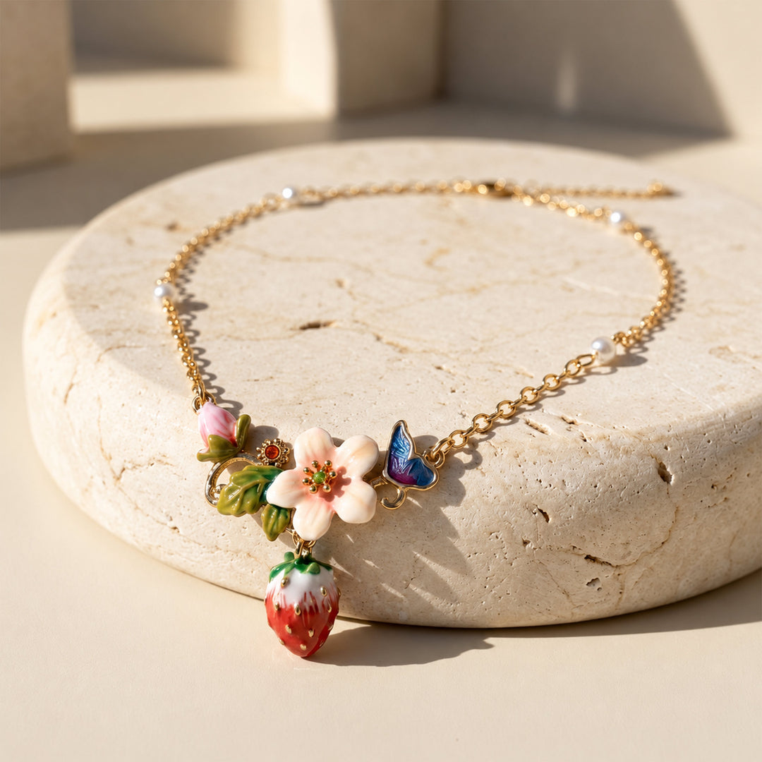 Hand-painted strawberry floral necklace with butterfly charm and pearl accents displayed on pale limestone.