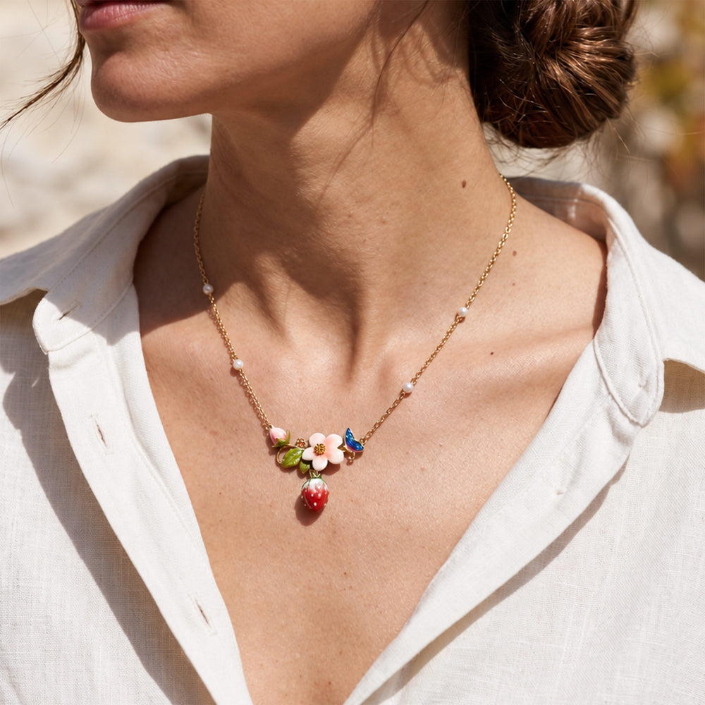 Model wearing a strawberry garden floral necklace with hand-painted flower and butterfly details outdoors.