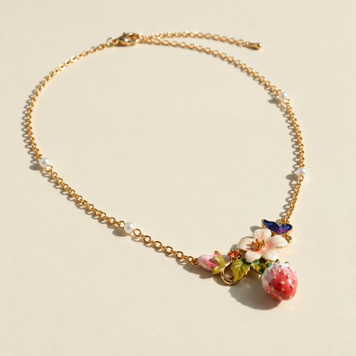 Strawberry garden floral necklace with pink flower, green leaves and butterfly detail on a sunlit cream surface